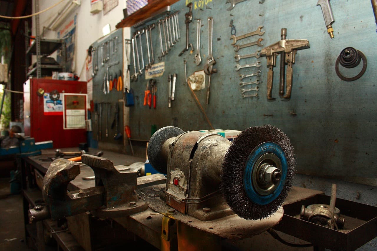 A workbench with a vice, a bench grinder and a wall of spanners