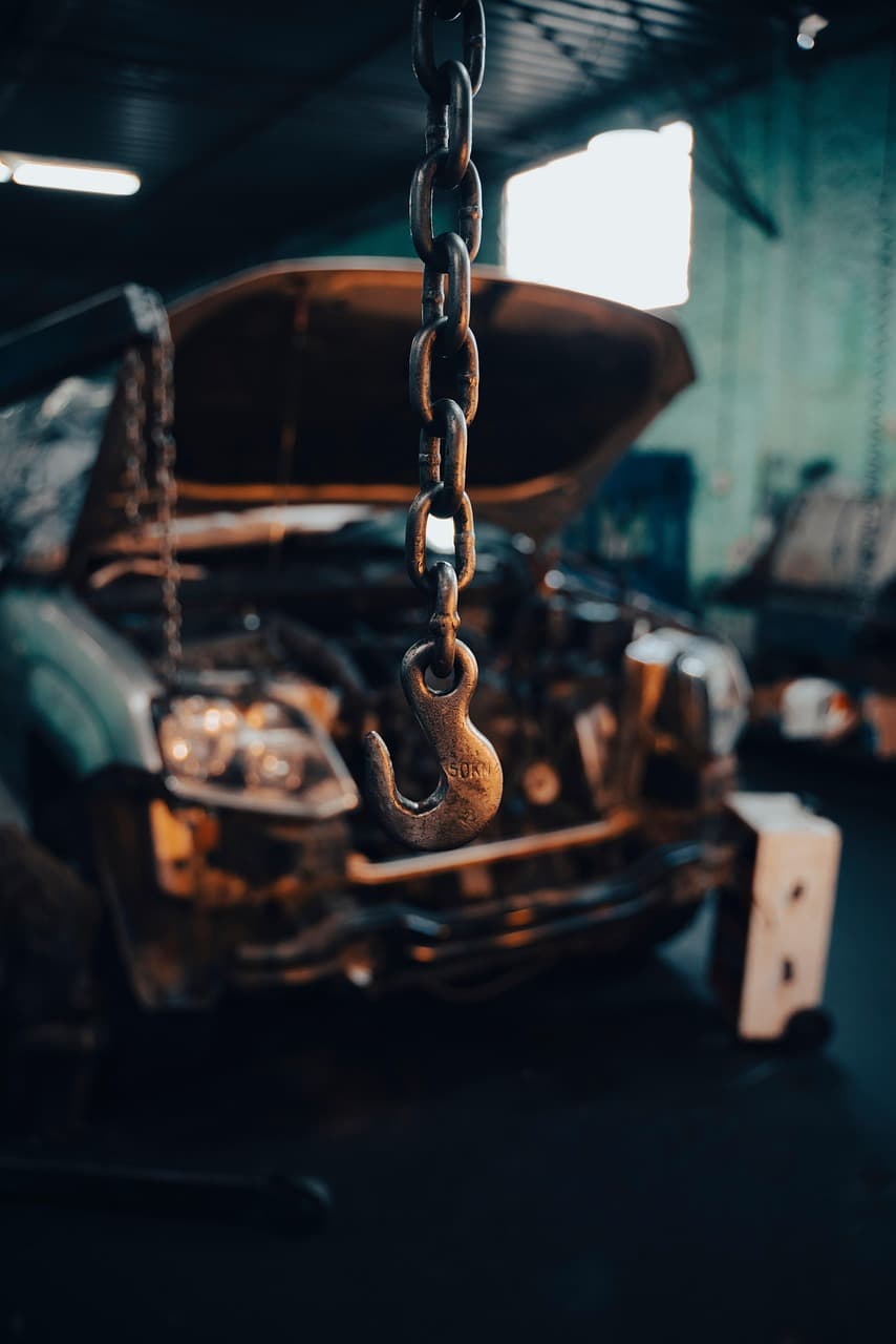An engine hoist chain hanging over an open engine bay in a dim workshop